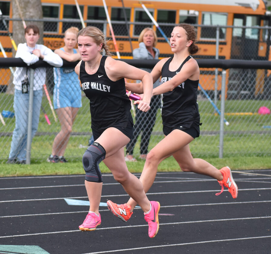 Staff photo by Ari Selvey River Valley’s Hailey Hollar takes the baton from teammate Brynne Ibberson in the girls 4x200-meter relay during the Tomahawk Conference track and field meet Thursday at Sleepy Eye High School.